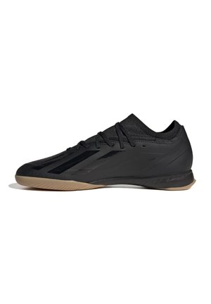 Chaussure de football indoor noire à coupe basse avec semelle en gomme et fermeture à lacets, vue de profil sur fond blanc.