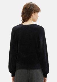 Zwarte, fluffy trui met lange mouwen en een ronde hals. Zachte textuur, iets losse pasvorm en minimalistisch design.