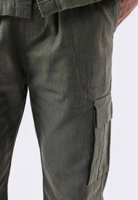 Pantaloni cargo verde oliva realizzati in tessuto testurizzato, con tasche laterali e dettagli ricamati sul fronte.