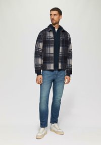 Chaqueta de cuadros en navy, gris y blanco con cierre de cremallera. Combinada con jeans azules y zapatillas blancas con acentos beiges.