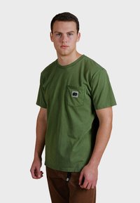 Zelené bavlněné tričko s krátkým rukávem, kulatým výstřihem a náprsní kapsou s logem medvěda. Hladká textura s uvolněným střihem.