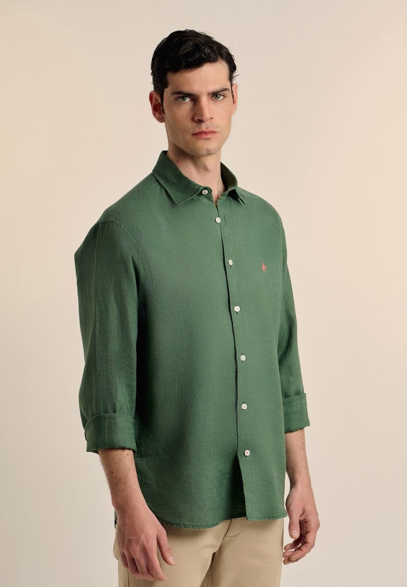 Camisa verde de botones en tejido ligero, con cuello, mangas largas arremangadas en los puños y un pequeño logo rojo en el lado izquierdo del pecho.