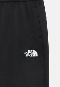 Juodi džinsai su baltu "The North Face" logotipu kairiajame šone, pagaminti iš lygaus, tekstūrinio audinio.