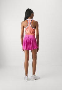 Top deportivo naranja con detalles azules y una falda plisada rosa. Zapatillas deportivas blancas completan el atuendo, diseñado para la ropa activa.