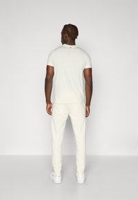 Lysfarvet, tætsiddende t-shirt med korte ærmer og rund halsudskæring, parret med matchende tapered bukser. Tekstureret stof, minimalistisk design.