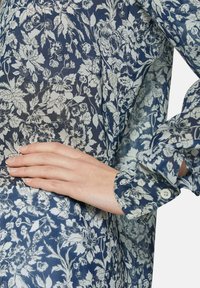 Bluse mit floralem Druck in Marineblau und Creme. Durchsichtiger Stoff mit einem zarten Muster, ausgestattet mit geknöpften Manschetten und einem lockeren Schnitt.