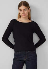 Black long-sleeve top with a round neckline, made of soft fabric. Paired with dark jeans featuring yellow stitching details.