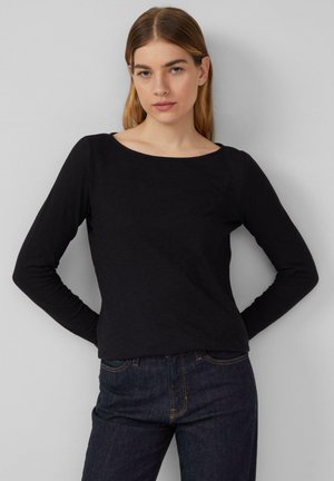 Zwarte longsleeve top met een ronde halslijn, gemaakt van zachte stof. Gecombineerd met donkere jeans met gele stikdetails.