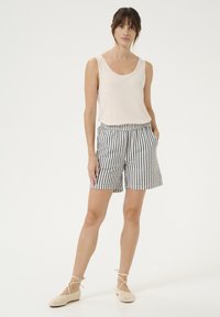 Top in beige chiaro con scollo rotondo, abbinato a pantaloni corti a righe bianche e nere con tasche laterali. La modella indossa delle ballerine color crema.