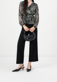 Schwarze Blumenshirtbluse mit durchsichtigen langen Ärmeln, kombiniert mit schwarzen weiten Hosen. Zubehör: kleine schwarze, gebogene Handtasche und Slingback-Absätze.