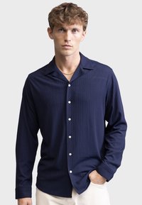 Navy long-sleeve shirt with vertical stripes, a notched collar, and five white buttons, made of a smooth, textured fabric.