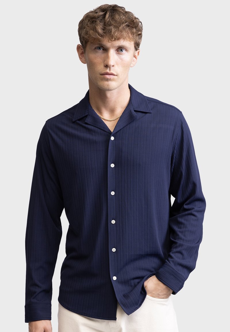 Navy long-sleeve shirt with vertical stripes, a notched collar, and five white buttons, made of a smooth, textured fabric.