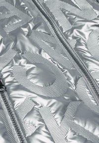 Silberne, gesteppte Jacke mit strukturierten Mustern und auffälliger Markenkennzeichnung, ausgestattet mit einem Doppelschluss und glattem, reflektierendem Stoff.