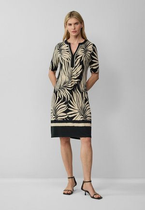Schwarz-creamfarbenes knielanges Kleid mit kurzen Ärmeln, das ein Palmenblattmuster und ein V-Ausschnitt-Design aufweist. Mit einem schwarzen unteren Saum akzentuiert.