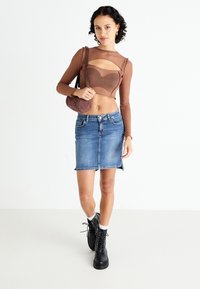 Brown long-sleeve top with cutout detail, blue denim skirt, black lace-up boots, and brown handbag with textured accents.