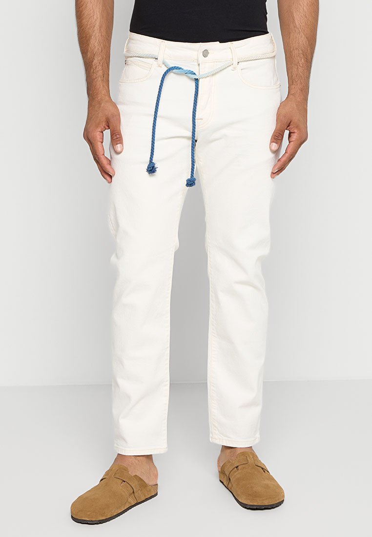 Pantalones de algodón blancos con pierna recta, con cordón azul y bolsillos frontales, llevados con zapatos marrones tipo slip-on.