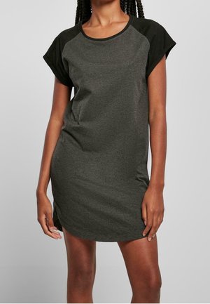 Kobieta ubrana w krótkim rękawem, ciemnoszary i czarny casualowy t-shirt w formie sukienki, stojąca na jednolitym tle.