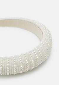 Fehér párnázott fejpánt, amelyet kicsi és nagy fényes gyöngyök díszítenek, textúrált mintázatban, létrehozva egy réteges hatást.