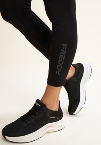 Leggings de sport noirs et baskets en maille noires avec semelles blanches. Les leggings présentent un logo réfléchissant sur le côté. Les baskets ont des tiges texturées.