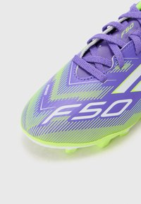 Scarpini da calcio viola e verdi con un motivo a zigzag, dotati di una superficie testurizzata, chiusura con lacci e un logo bianco che recita "F50."