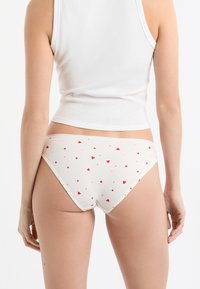 Weiße gerippte Bikinihöschen mit einem verstreuten Muster aus roten und pinken Herzen, samt einer weichen Textur und einem niedrigen Bund.