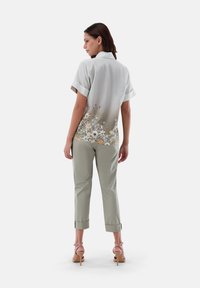 Hellegraues Kurzarmhemd mit Blumendruck am Saum, kombiniert mit hellgrünen, verkürzten Hosen und beigen, hochhackigen Sandalen.