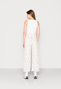 Top branco sem mangas combinado com calças largas de cintura alta em bege claro, com um padrão de flores azuis. Calçado: sapatos brancos e pretos.