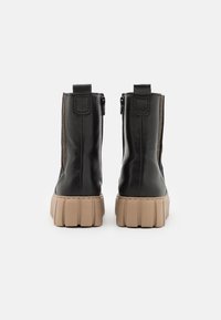 Bottines en cuir noir avec un panneau latéral texturé, semelle épaisse beige et fermeture éclair à l'arrière.