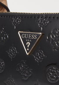 Zwarte geëmbosseerde handtas met een driehoekig metalen logo met "GUESS USA" en een vraagteken. Textuur oppervlak met een subtiel patroon.