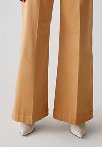 Pantaloni a gamba larga marrone chiaro con texture liscia, caratterizzati da un orlo pulito e décolletés beige a punta con finitura lucida.