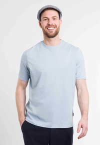 T-shirt bleu clair à manches courtes avec un col rond, texture lisse et accents latéraux. Porté avec un pantalon sombre et une casquette plate grise.