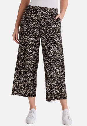 Weite, gekürzte Hosen mit einem schwarz-beigen abstrakten geometrischen Muster, kombiniert mit weißen Turnschuhen und einem in die Hose gesteckten weißen Oberteil.