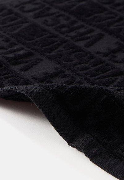 Gros plan d'un tissu noir texturé avec des motifs géométriques en relief sur un bord plié sur fond blanc.