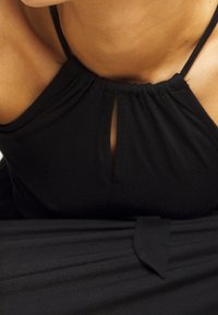 Czarna sukienka z dekoltem w kształcie klucza, marszczonym materiałem i regulowanymi ramiączkami. Miękka tekstura z węzłem na wysokości talii.