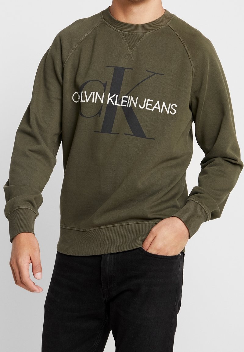 Olivově zelená bavlněná mikina s velkým černým logem "CK" a textem "CALVIN KLEIN JEANS" v bílé barvě, s žebrovanými manžetami a lemem.