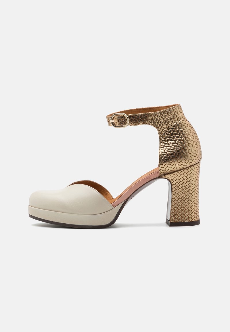 Escarpin fermé avec avant beige, bride de cheville texturée dorée métallique et talon bloc, avec une fermeture à boucle latérale.