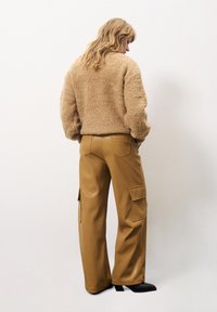 Tan fluweelachtig sweater met een ronde hals, gecombineerd met hoge, bruine wijde cargobroek met zijzakken. Zwarte schoenen maken de look compleet.