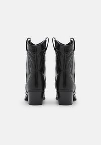 Para czarnych skórzanych kowbojek z haftowanymi wzorami dekoracyjnymi i uchwytami do zakupu, widzianych z tyłu na białym tle.