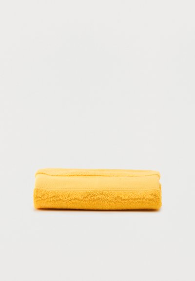 Διπλωμένη κίτρινη πετσέτα από περκάλ τοποθετημένη επίπεδα σε απλό λευκό φόντο.