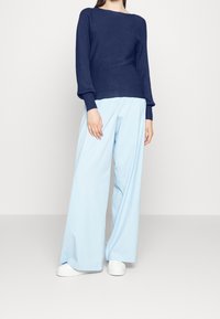 Granatowy sweter z prążkowanej dzianiny o szerokich rękawach, zestawiony z jasnoniebieskimi spodniami typu wide-leg i białymi trampkami. Gładkie tekstury i luźny krój.