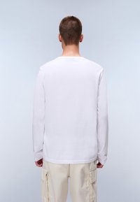 Hvid langærmet T-shirt med rund hals, lavet af bomuld. Har en afslappet pasform og bæres med lysebeige cargo-bukser.