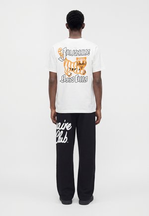 Mand set bagfra iført en hvid t-shirt med en orange tiger og teksten "Billionaire Boys Club" samt sorte bukser med hvid skrift.