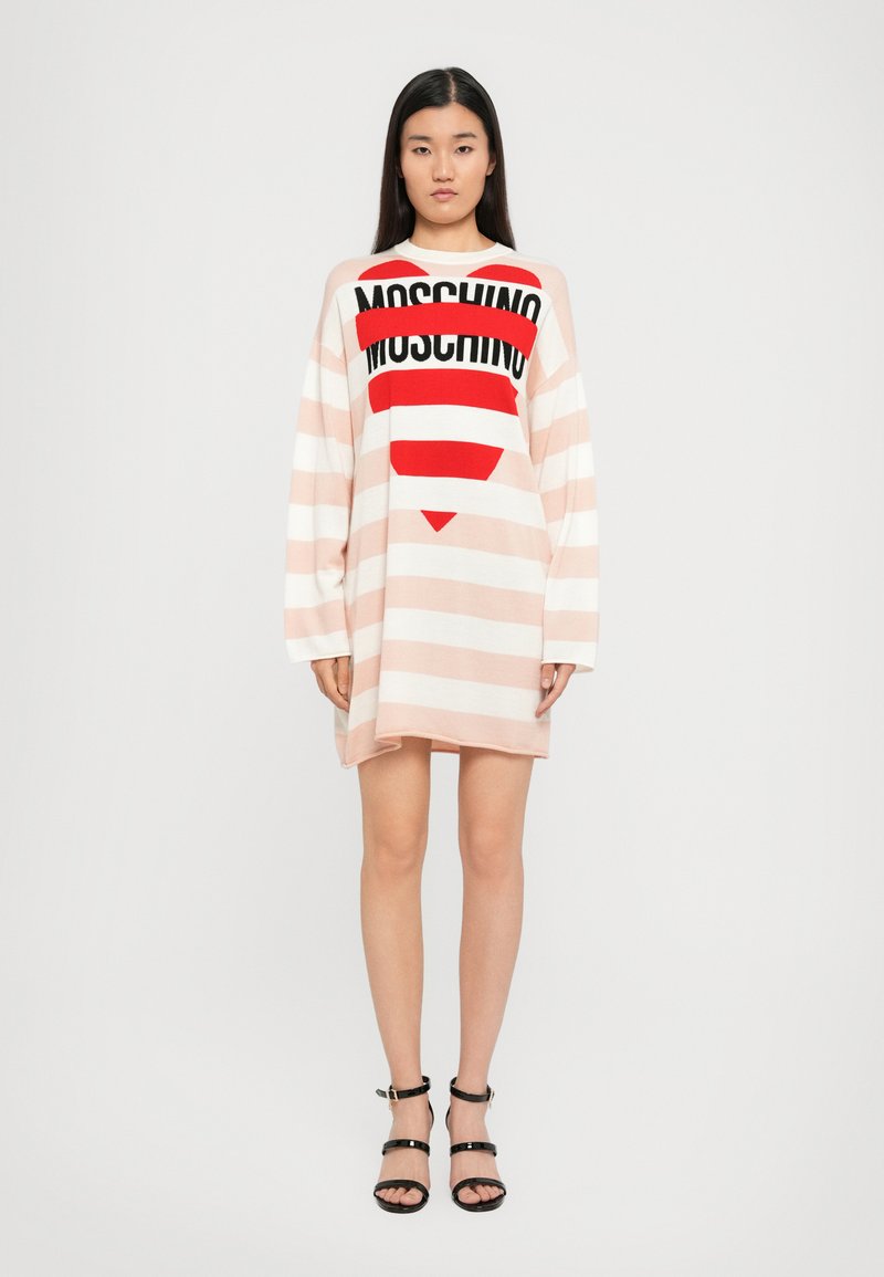 Abito lungo oversized a righe in rosa pallido e bianco, con logo nero e grafica di cuore rosso. Maniche lunghe e vestibilità rilassata.