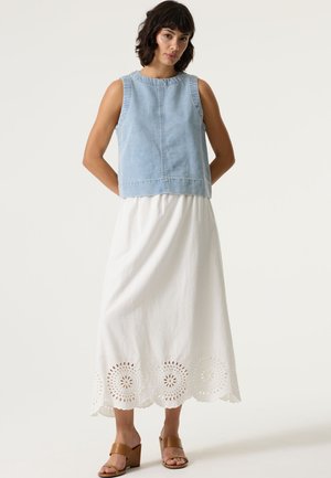 Haut en denim sans manches avec un col rond, associé à une longue jupe blanche ornée de motifs floraux découpés à l'ourlet. Sandales compensées marron.