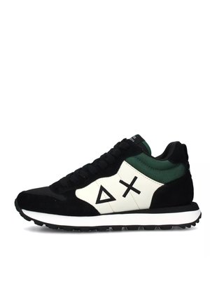 Scarpa sportiva in scamosciato nero con dettagli bianchi. Presenta un tab sul tallone verde, loghi geometrici neri e una suola in gomma testurizzata.