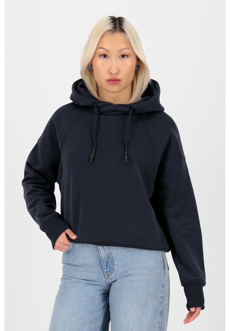 Felpa cropped blu navy realizzata in tessuto morbido, caratterizzata da un ampio cappuccio, cordini regolabili e polsini a costine. Abbinata a jeans blu chiaro.
