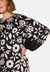 Mustat kankaatoppi, jossa on suuria vaaleanpunaisia kukka- ja lehtikuvioita, pyöreä kaula-aukko ja kerätty, joustava hihansuu.