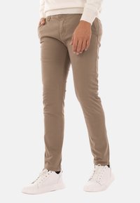 Pantaloni beige slim-fit con tasche laterali, realizzati in morbido tessuto di cotone, abbinati a scarpe da ginnastica bianche con lacci.