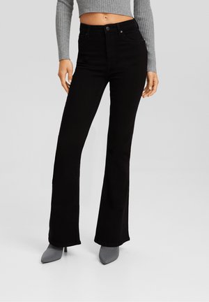 Black flared jeans made of soft denim. High-waisted design with front pockets and a fitted waist, paired with gray heeled ankle boots.