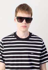 Black square sunglasses with dark lenses, worn with a black and white striped t-shirt featuring a small "MN" logo on the left side.